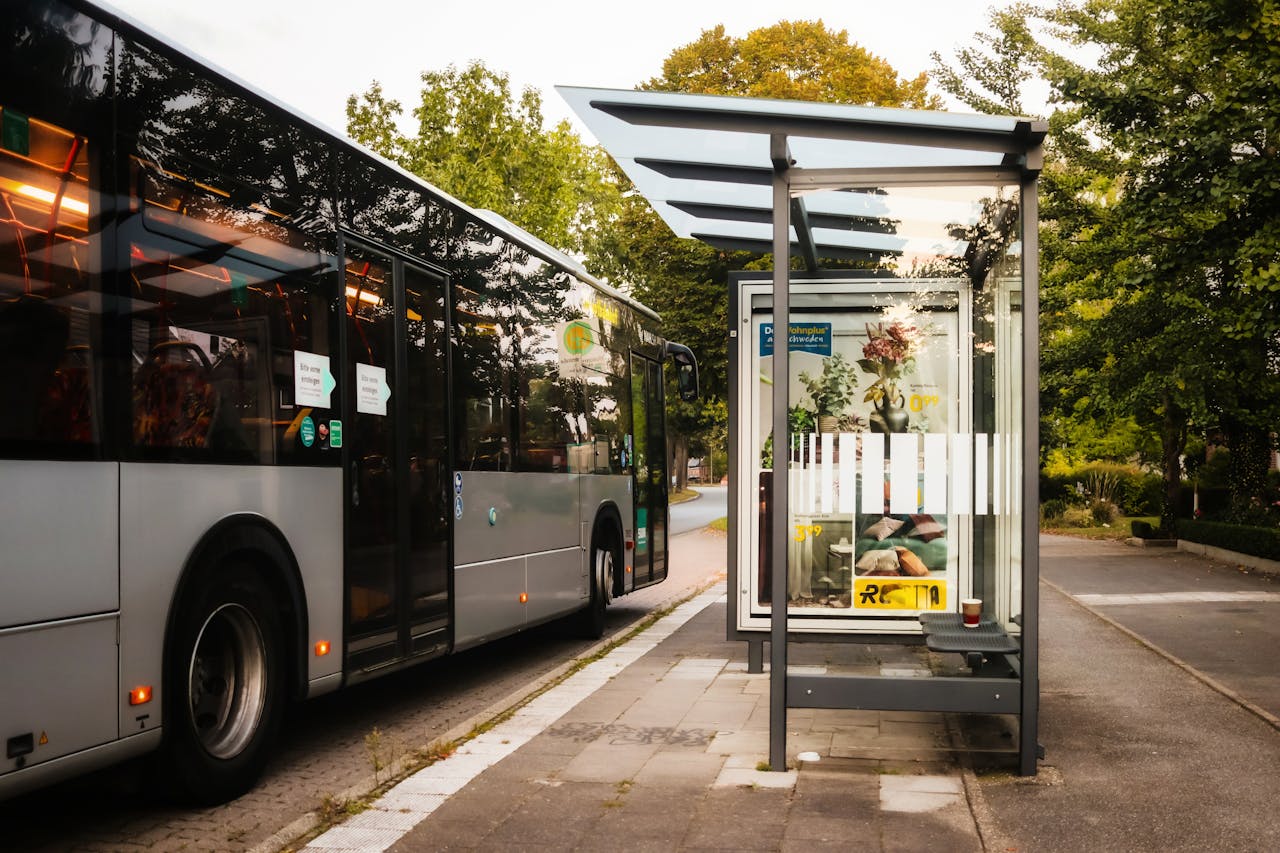 Modern city bus at a glass bus stop during summer, showcasing urban transportation and greenery.